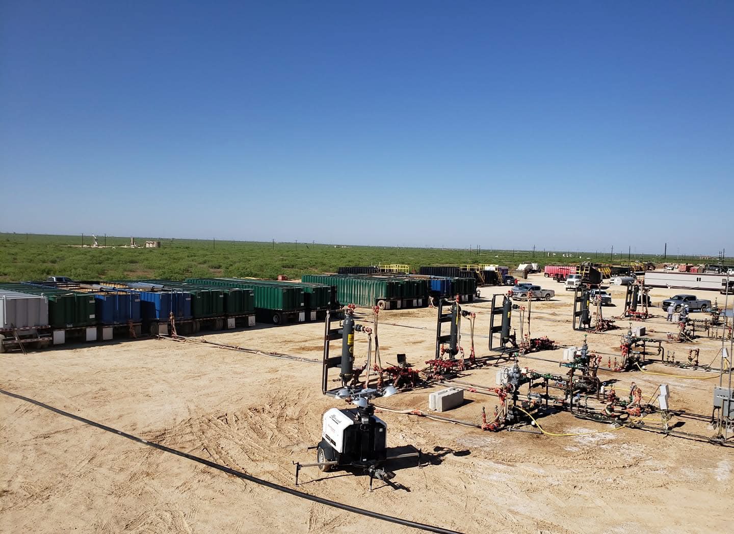 A vast field with multiple oil or gas wellheads under a clear blue sky.