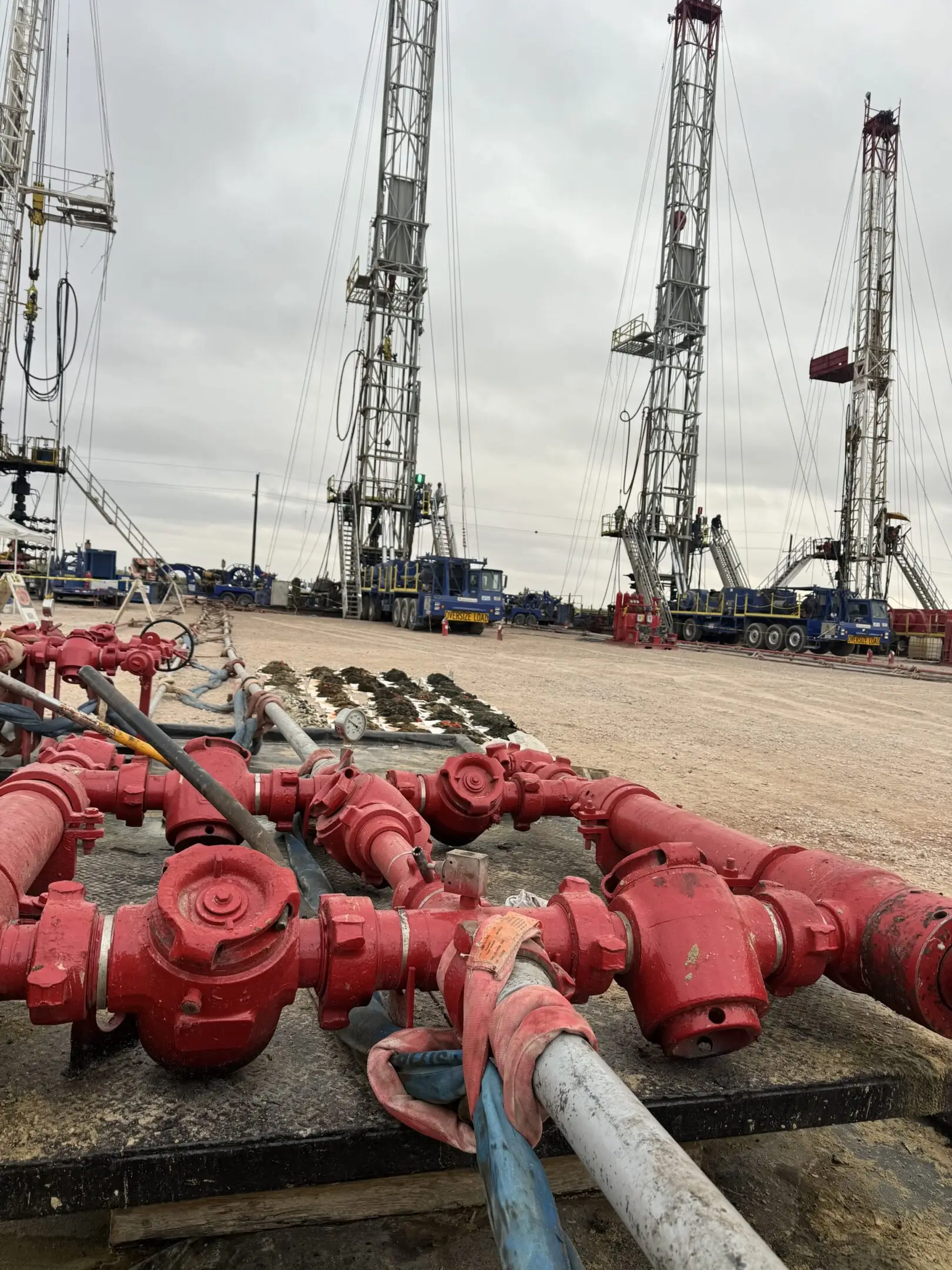 Oilfield equipment and wellheads lined up with drilling rigs in the background.
